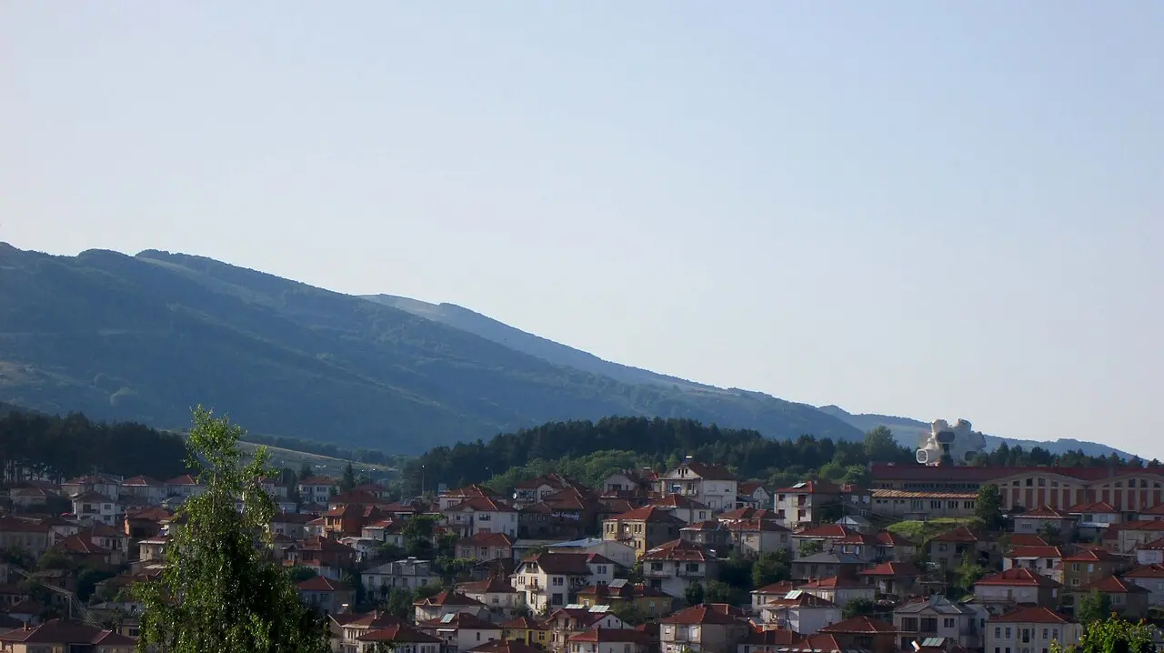 The red-roofed houses of Kruševo climbing a steep hillside beneath a mountain, with the white Makedonium monument on the ridge