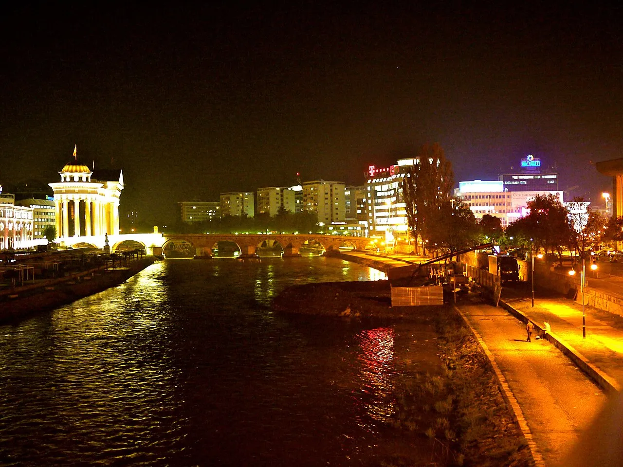 Skopje skyline at night along the Vardar river, with the Stone Bridge and lit office buildings